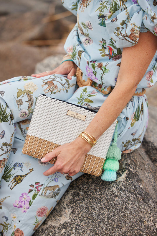 Person holding a woven clutch with tassel details, wearing a floral dress.