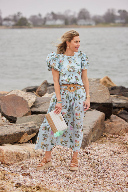 Woman in a floral dress standing by a body of water with rocks.