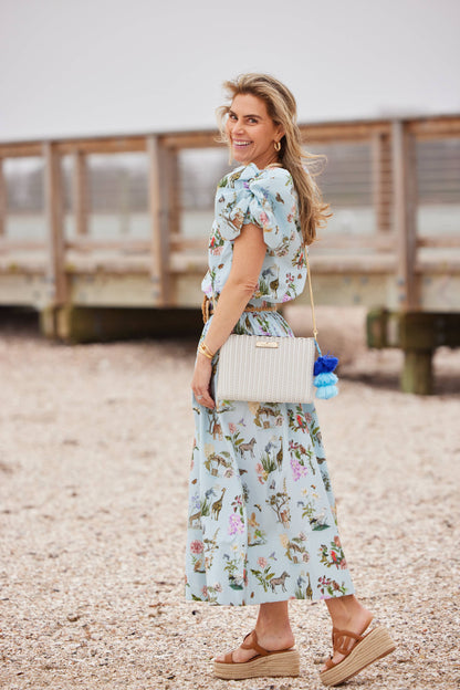 Woman in a floral dress standing on a pebbly beach with a wooden walkway in the background.