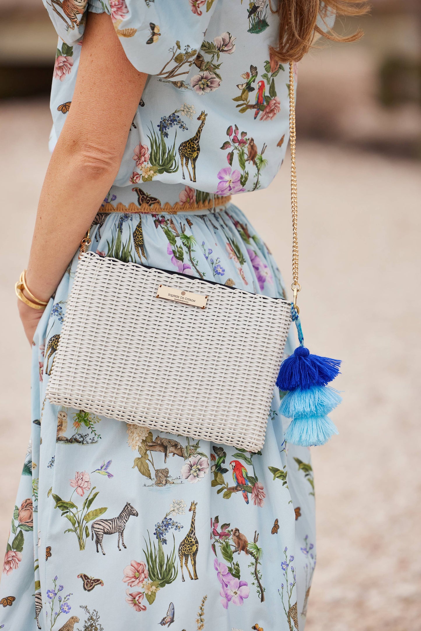 Woman wearing a floral dress with a woven handbag featuring blue tassels.