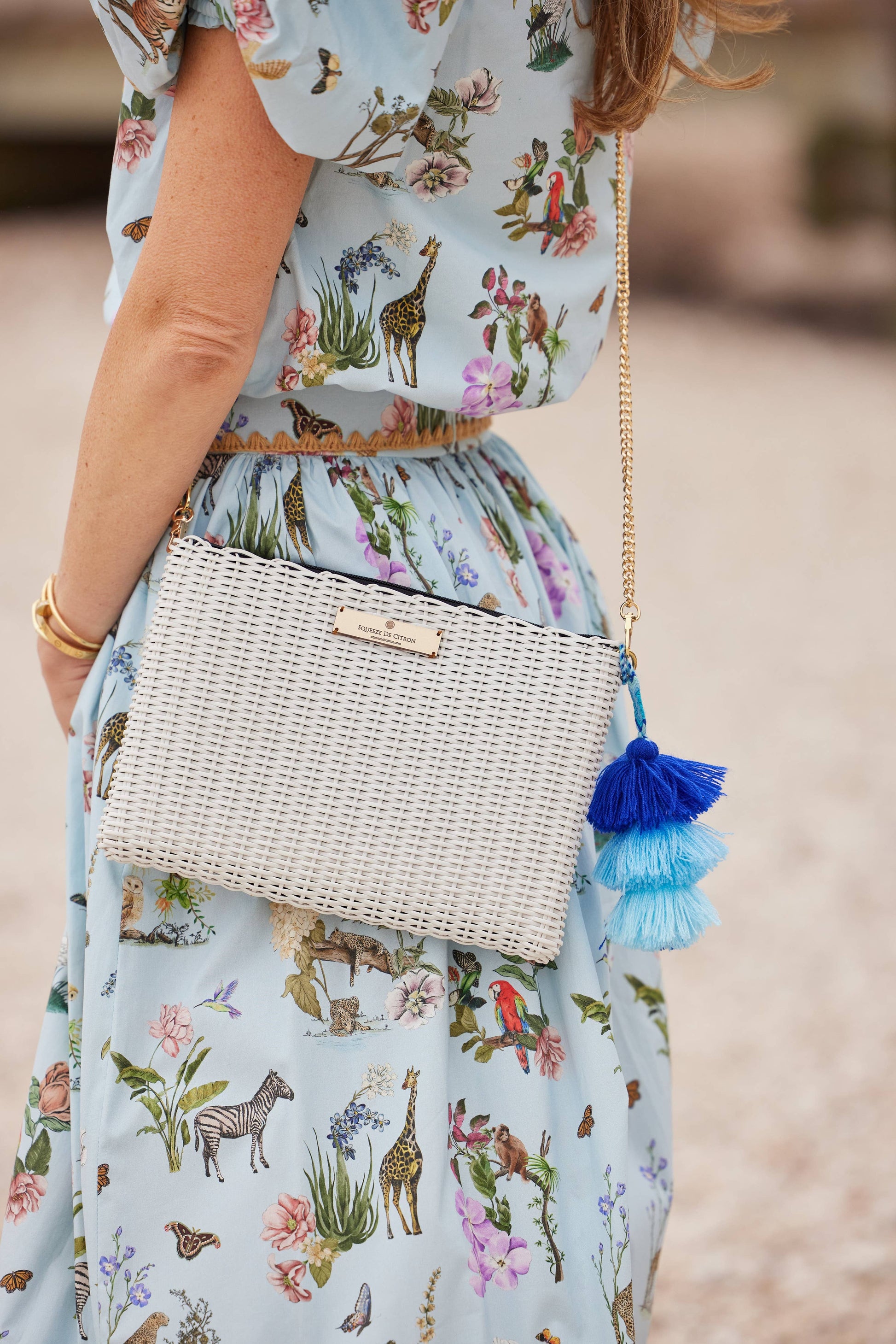 Woman wearing a floral dress with a woven handbag featuring blue tassels.