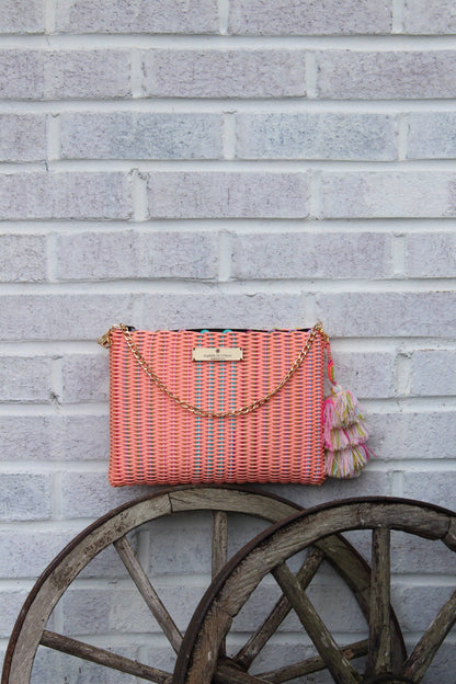 Pink woven handbag with tassels hanging on a brick wall