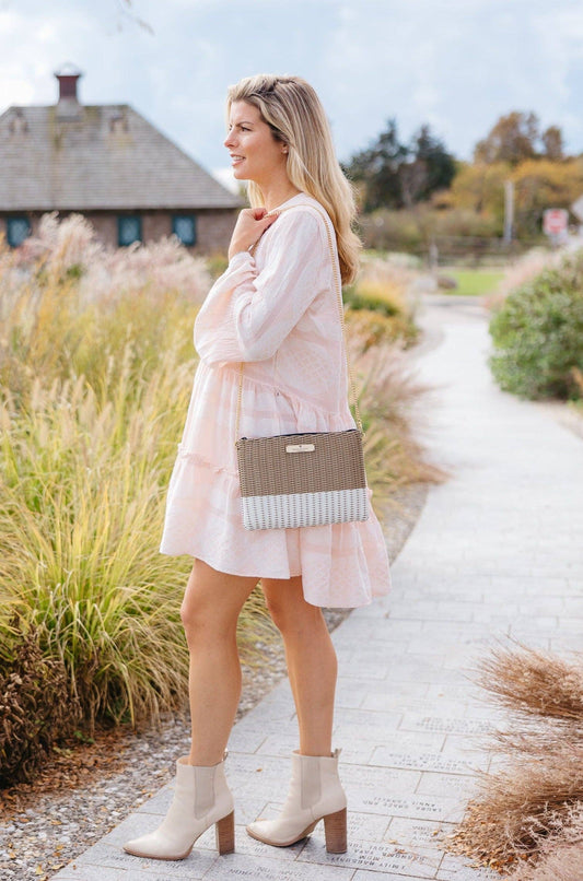 Woman in a white dress with a beige handbag walking on a path in a garden.