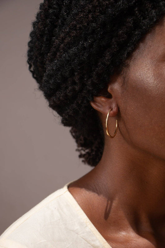 Close-up of a person wearing a gold hoop earring with a neutral background