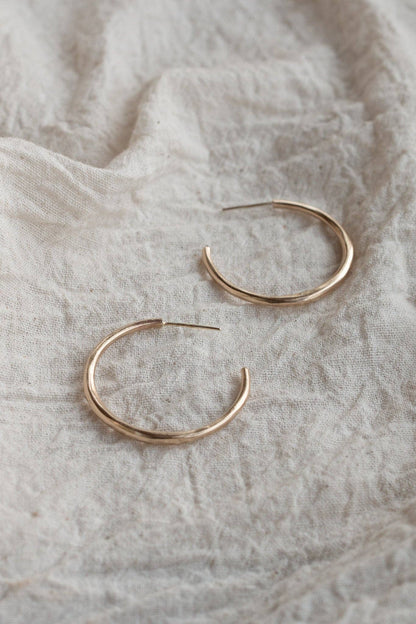 Gold hoop earrings on a textured beige fabric background