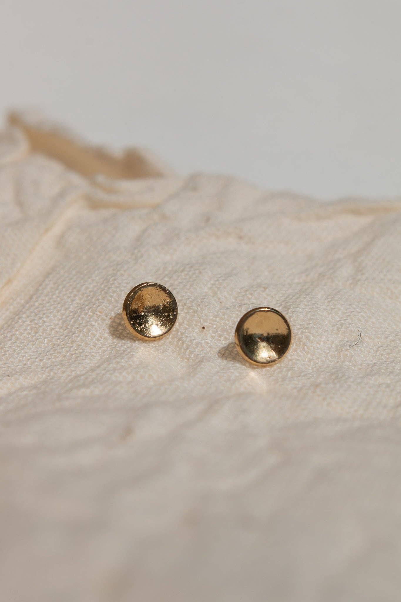 Pair of gold stud earrings on a textured beige surface