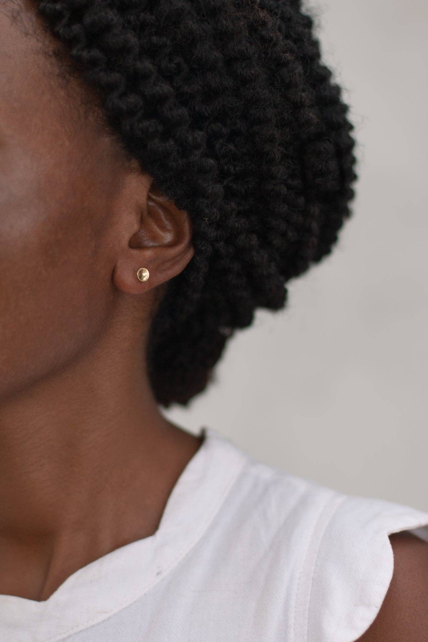 Close-up of a person wearing a gold earring with a plain background