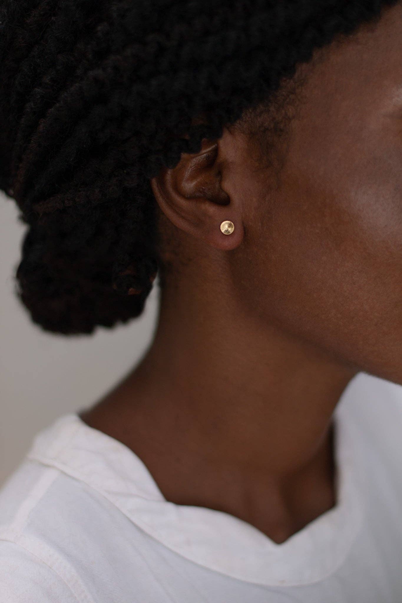 Close-up of a person wearing gold earrings with a plain background