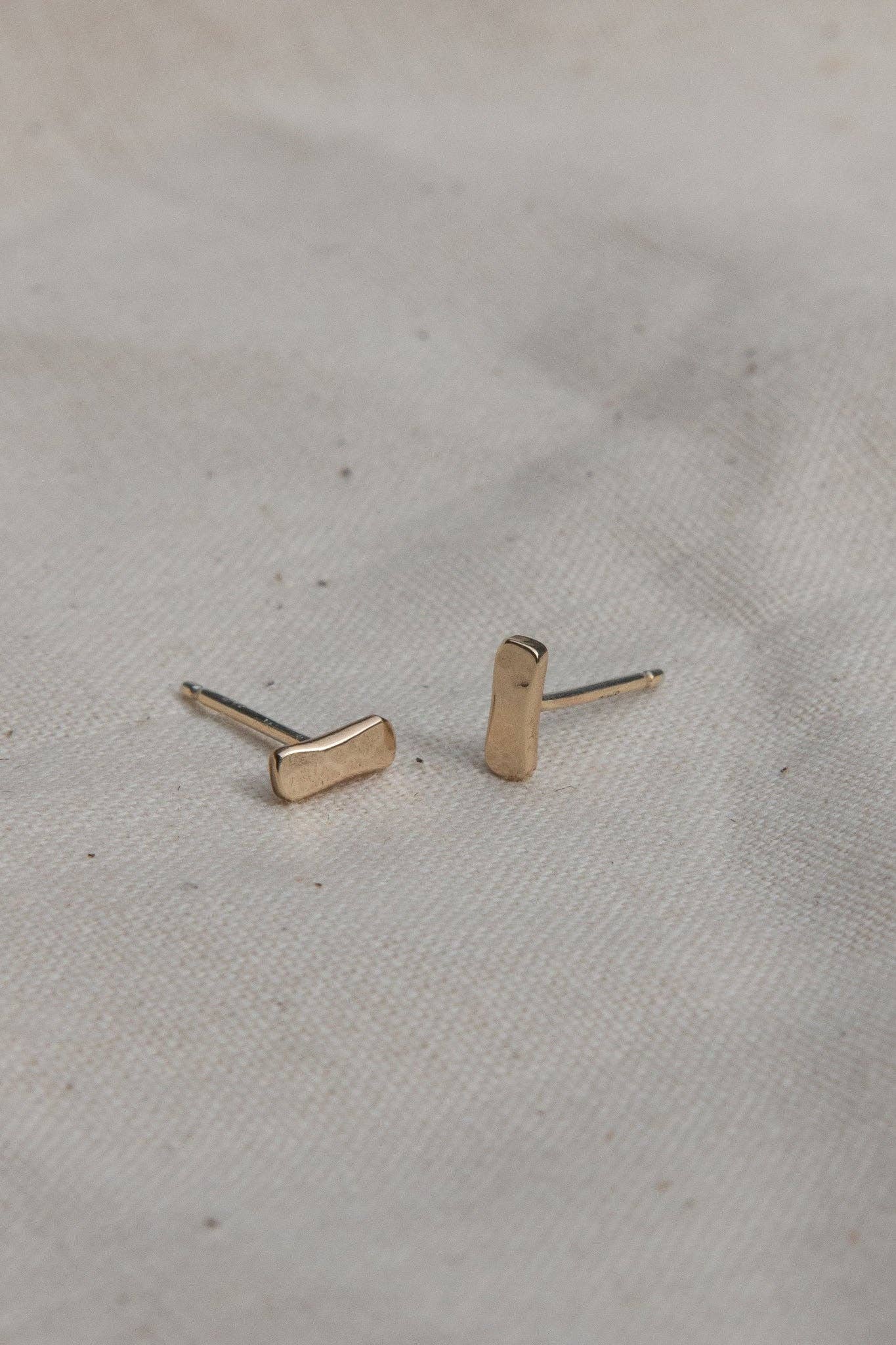 Gold bar-shaped earrings on a light fabric background