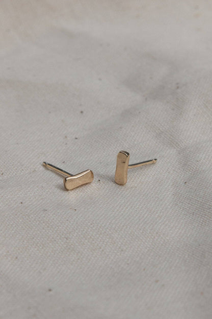 Gold bar-shaped earrings on a light fabric background