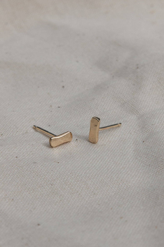 Gold bar-shaped earrings on a light fabric background