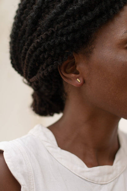 Close-up of a person wearing gold earrings with a neutral background