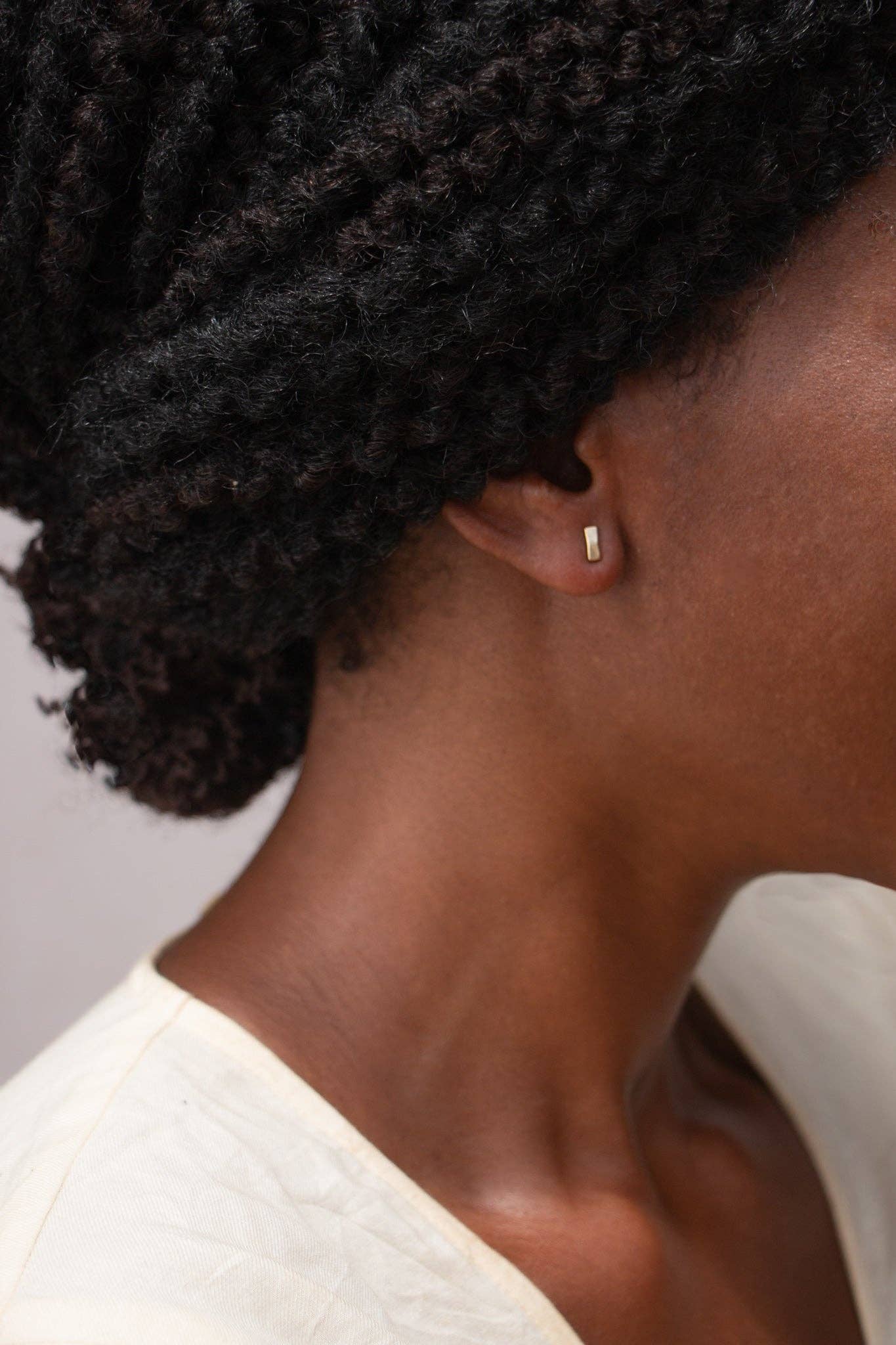 Close-up of a person wearing a gold earring with a plain background