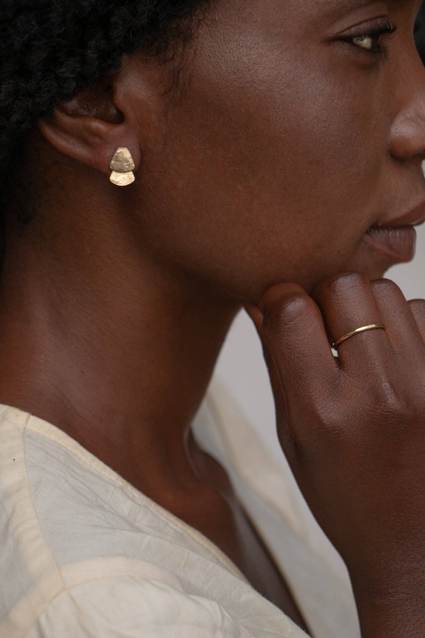 Close-up of a person wearing gold earrings and a ring, with a neutral background
