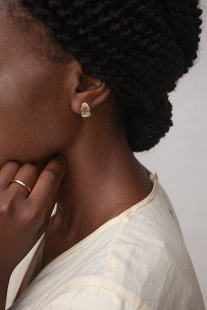 Close-up of a person wearing gold earrings and rings with a neutral background