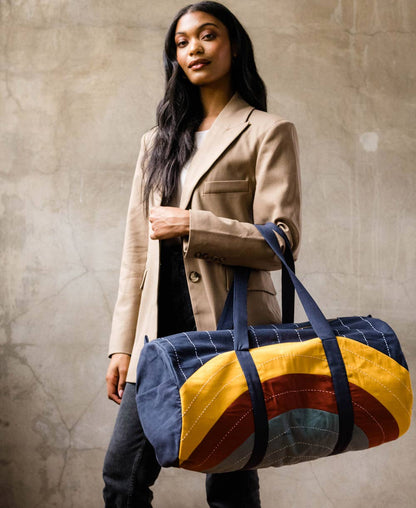 Woman holding a colorful duffel bag against a neutral background