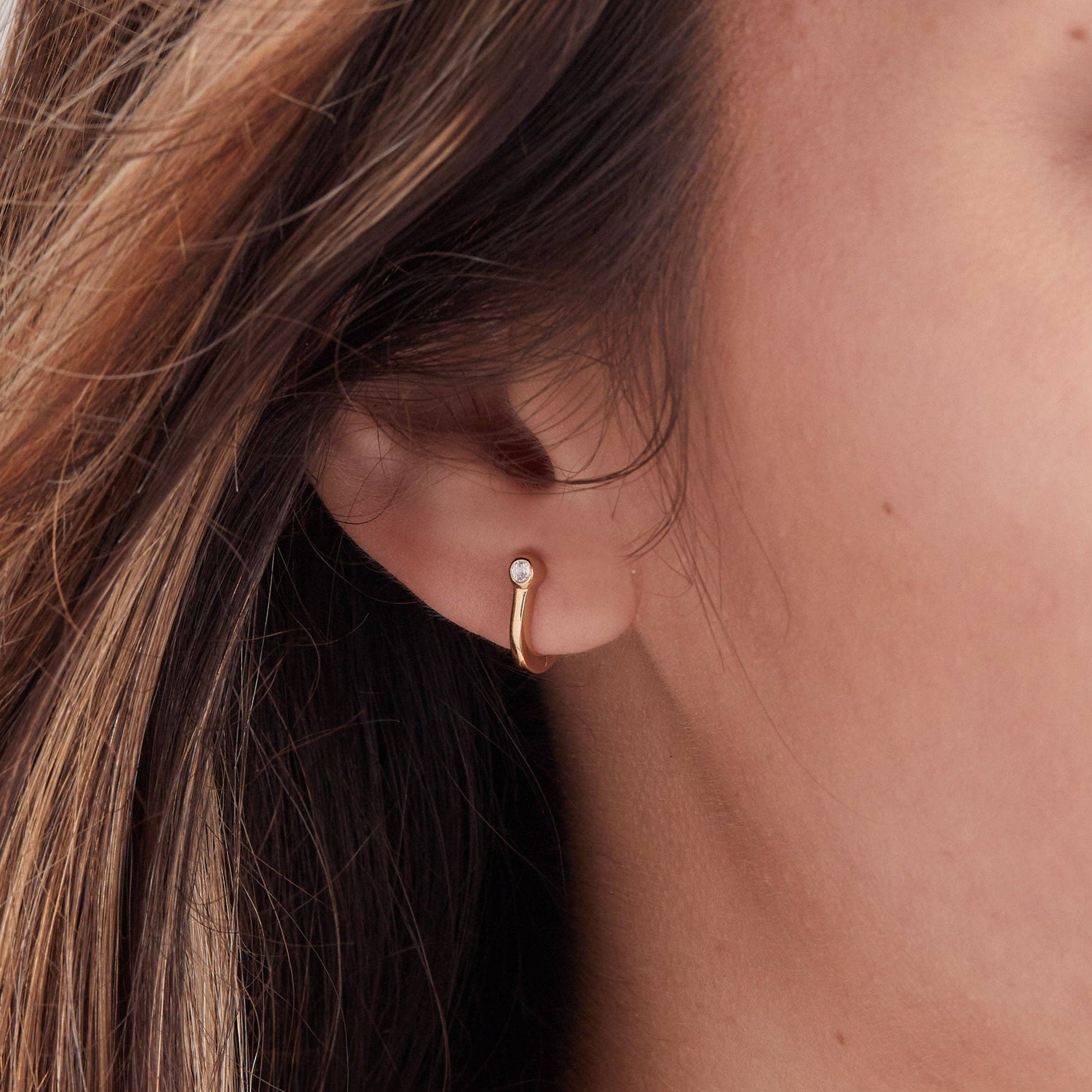 Close-up of a person wearing a gold hoop earring with a small gemstone.