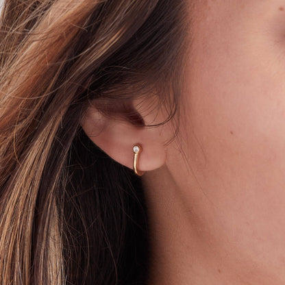 Close-up of a person wearing a gold hoop earring with a small gemstone.