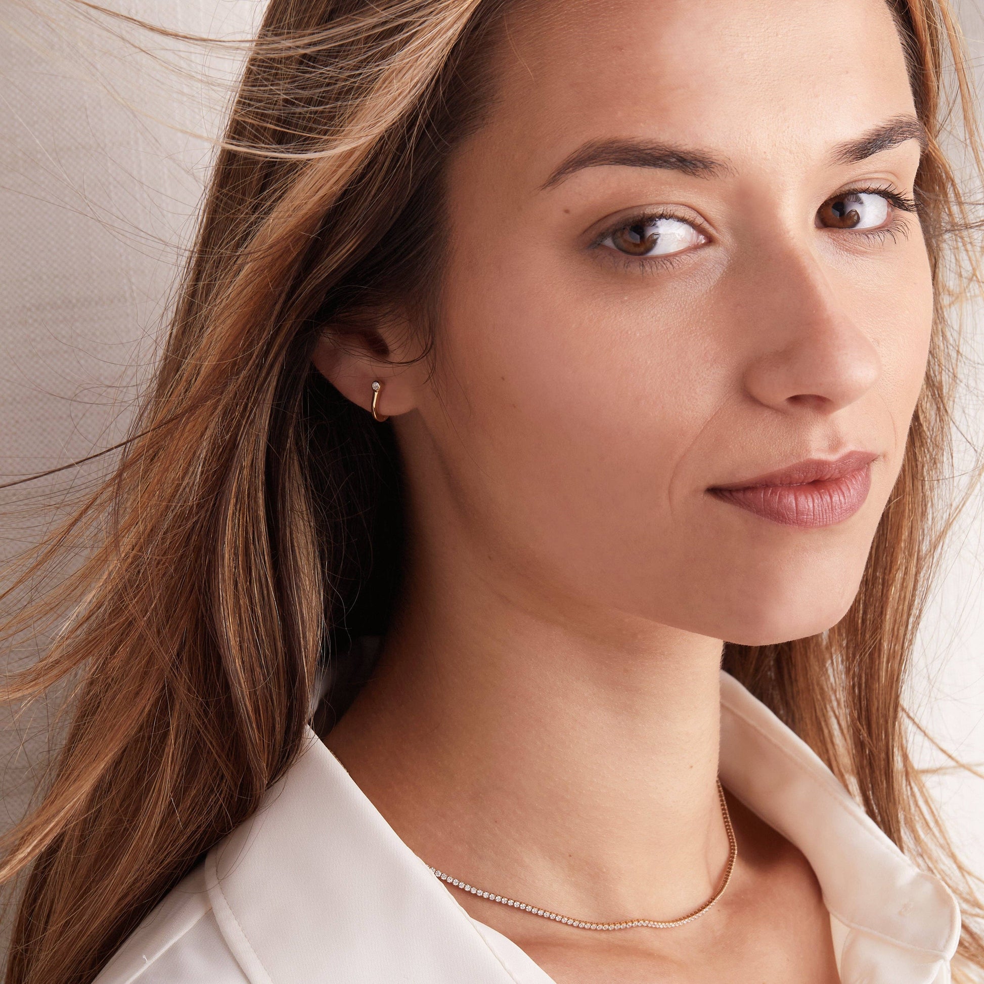 Close-up of a woman wearing a gold earring and necklace against a neutral background