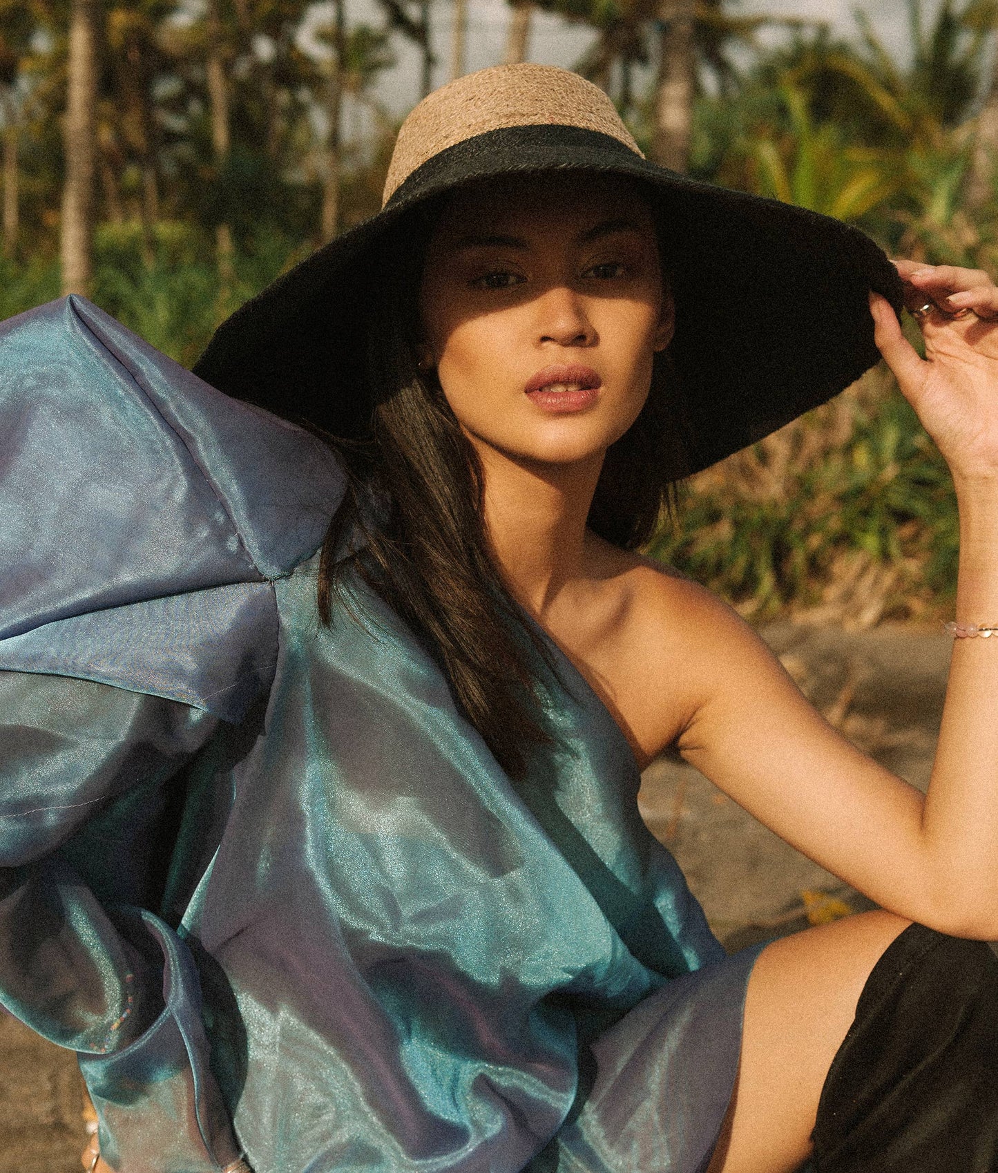 Woman wearing a large black hat and a blue and gray patterned dress outdoors.