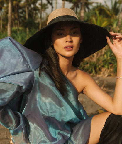 Woman wearing a large black hat and a blue and gray patterned dress outdoors.