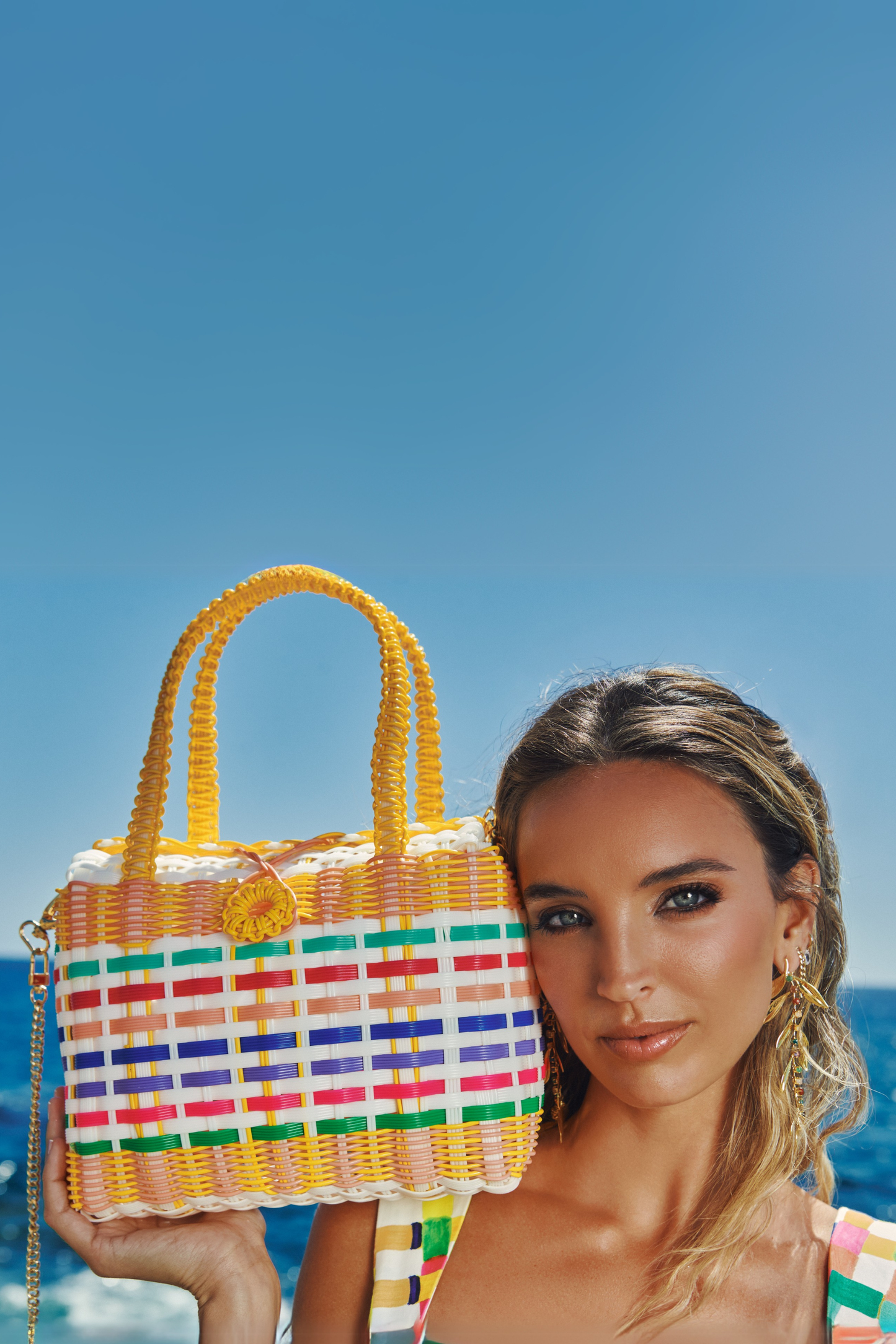 Woman holding a colorful woven handbag against a clear blue sky.