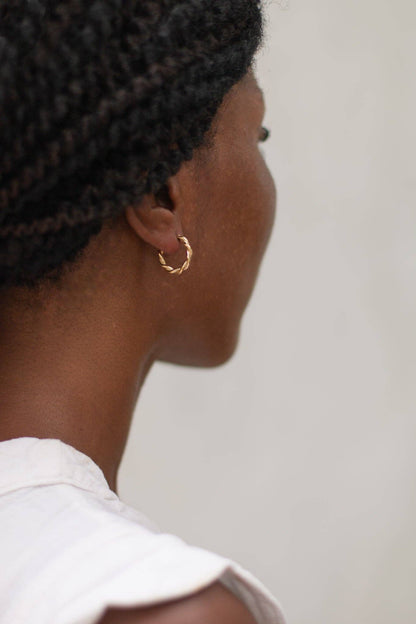 Person wearing a black knitted headband and gold hoop earring against a plain background