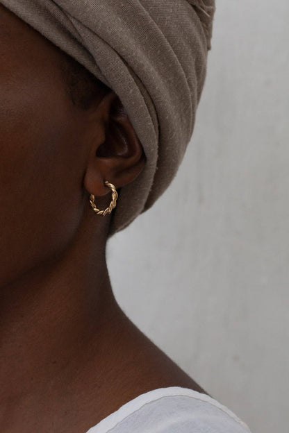 Close-up of an ear wearing a gold hoop earring with a neutral background