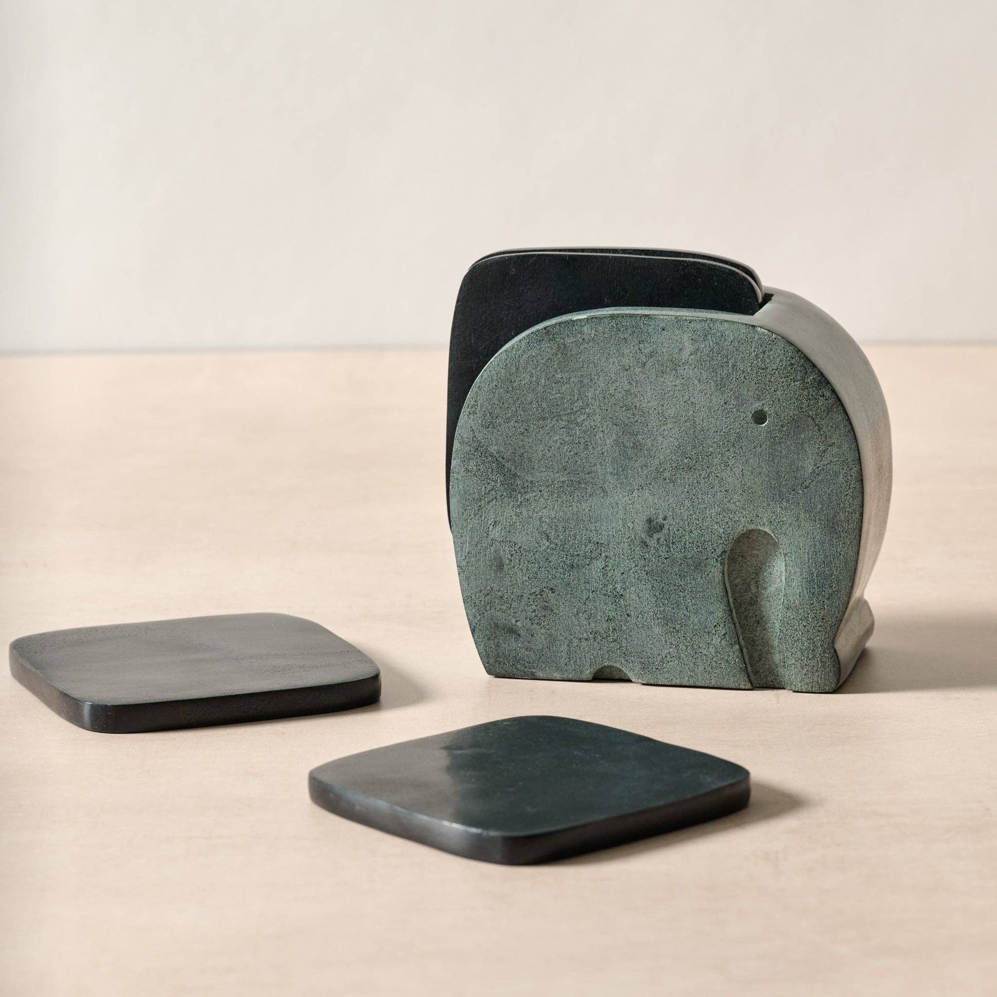 Set of stone coasters, including a large elephant-shaped coaster, on a beige surface.