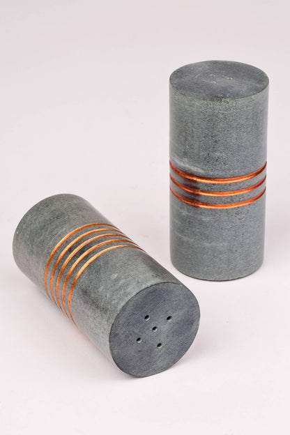 Two cylindrical stone salt shakers with copper bands on a white background