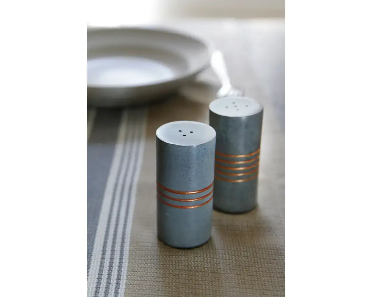 Two gray salt and pepper shakers with copper stripes on a table.