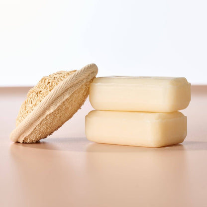 Two bars of soap and a loofah on a light surface