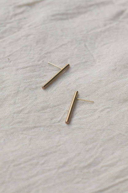 Gold bar earrings on a textured beige fabric background