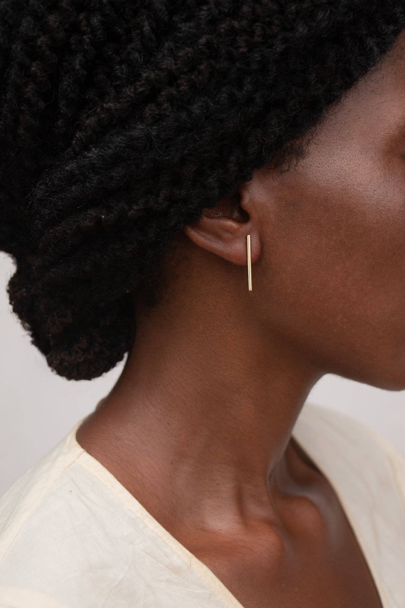 Close-up of a person wearing a gold hoop earring with a plain background