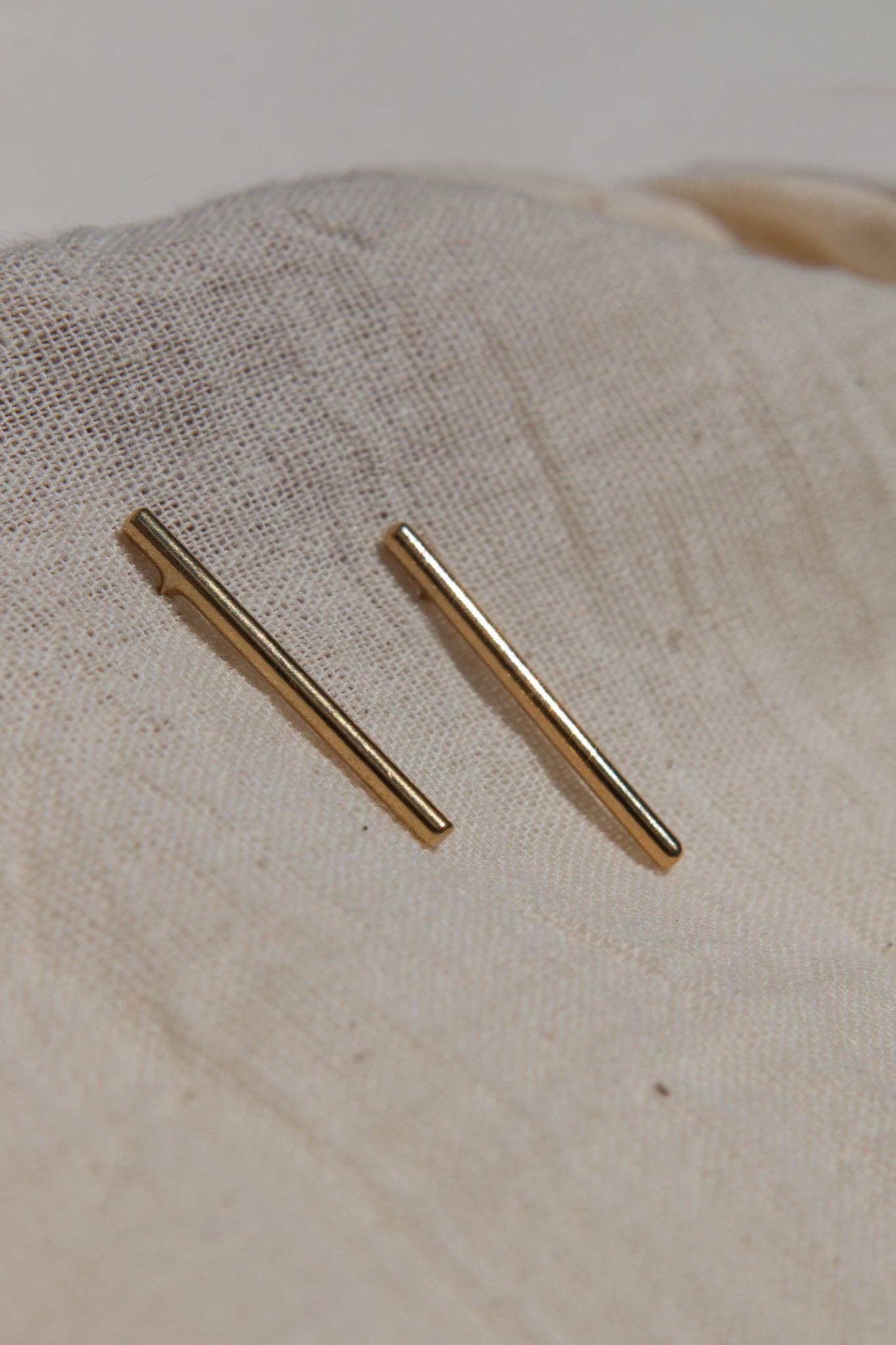 Two gold bar earrings on a beige fabric background