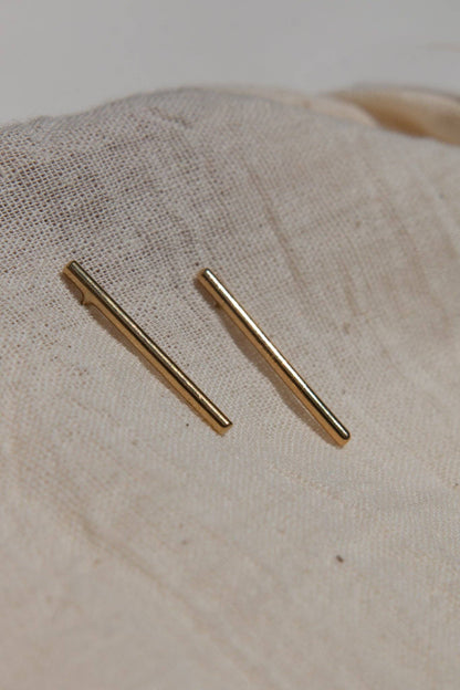 Two gold bar earrings on a beige fabric background