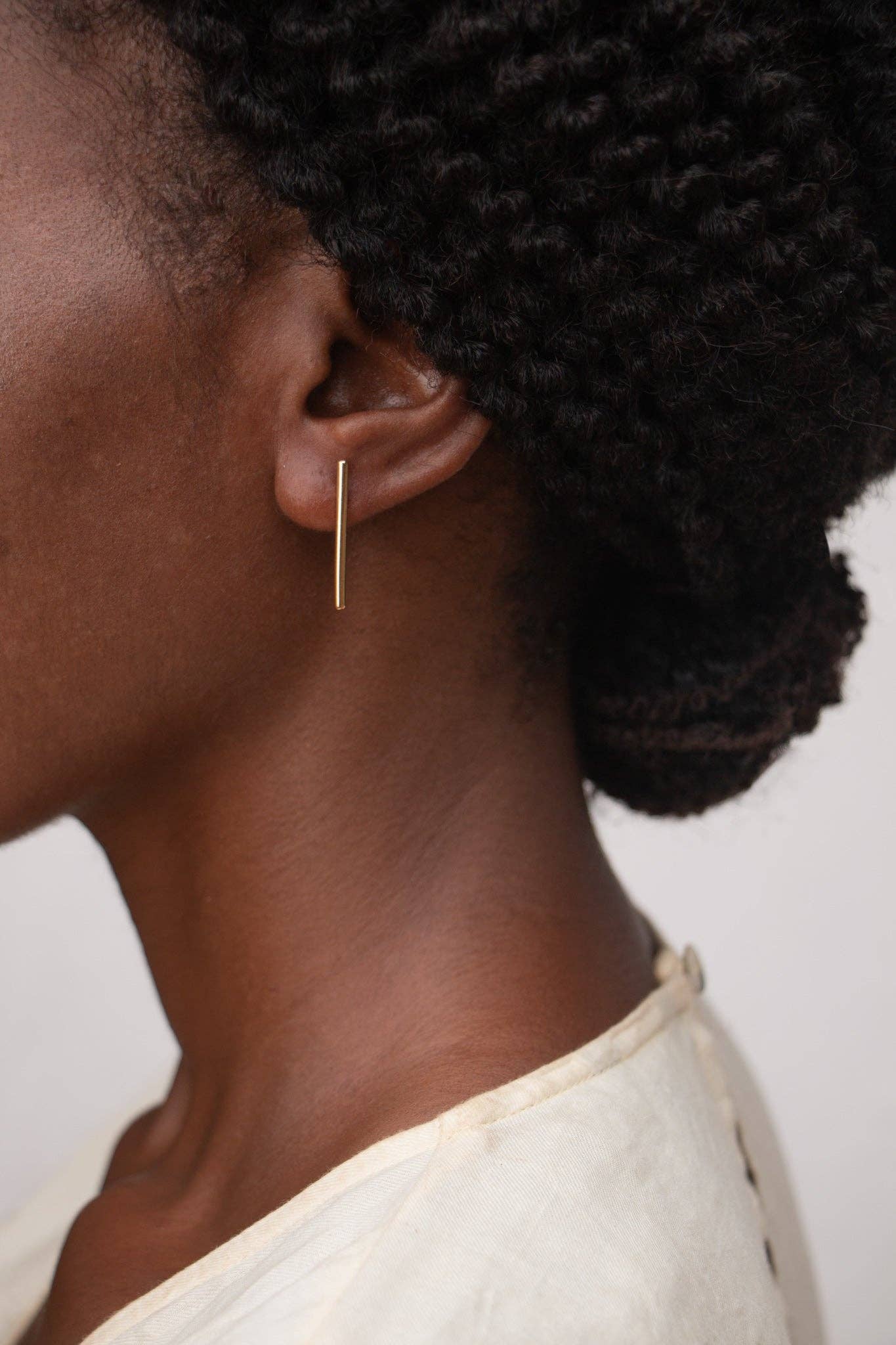 Close-up of an ear wearing a gold hoop earring with a plain background