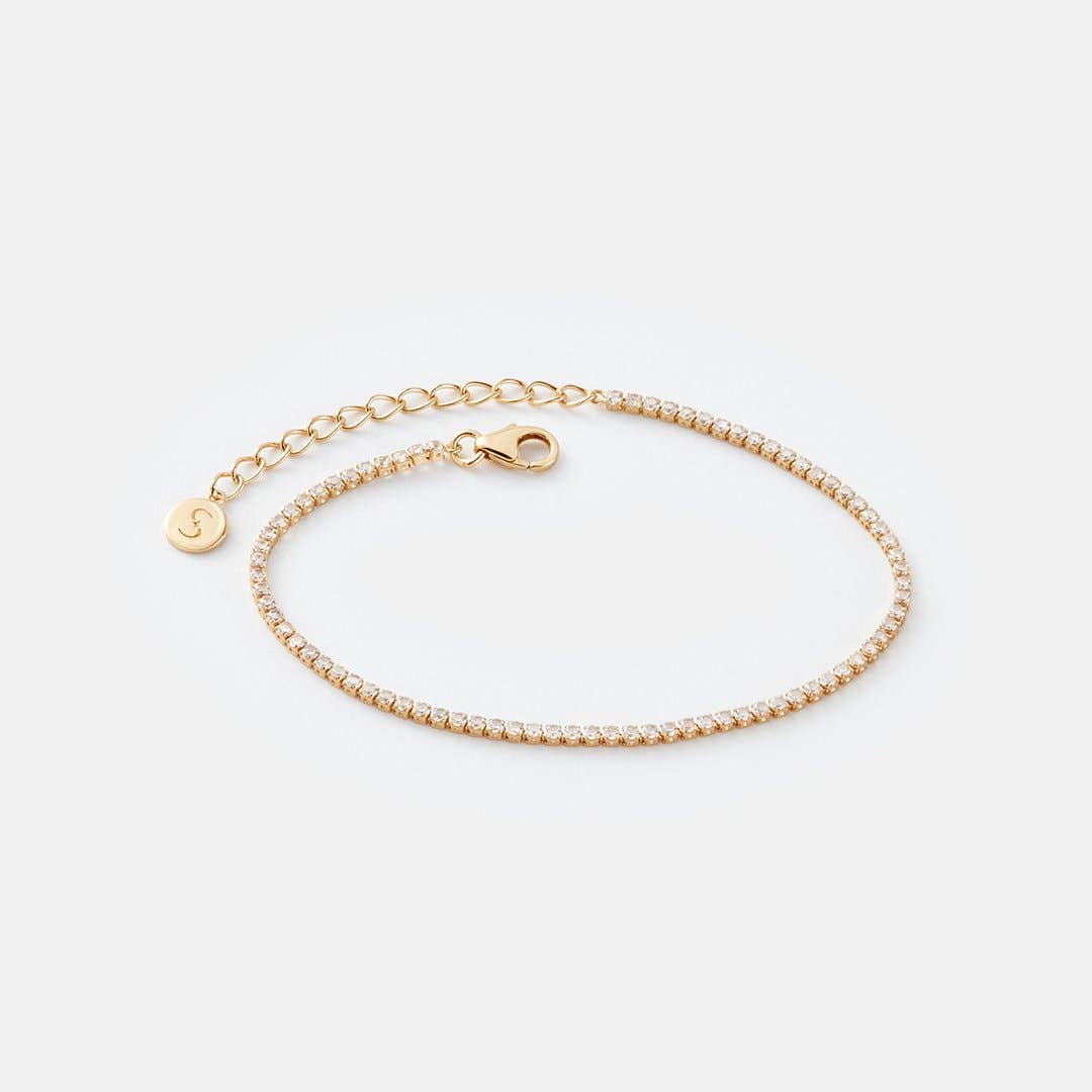 Gold bracelet with a small round charm on a light gray background