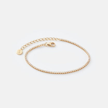 Gold bracelet with a small round charm on a light gray background