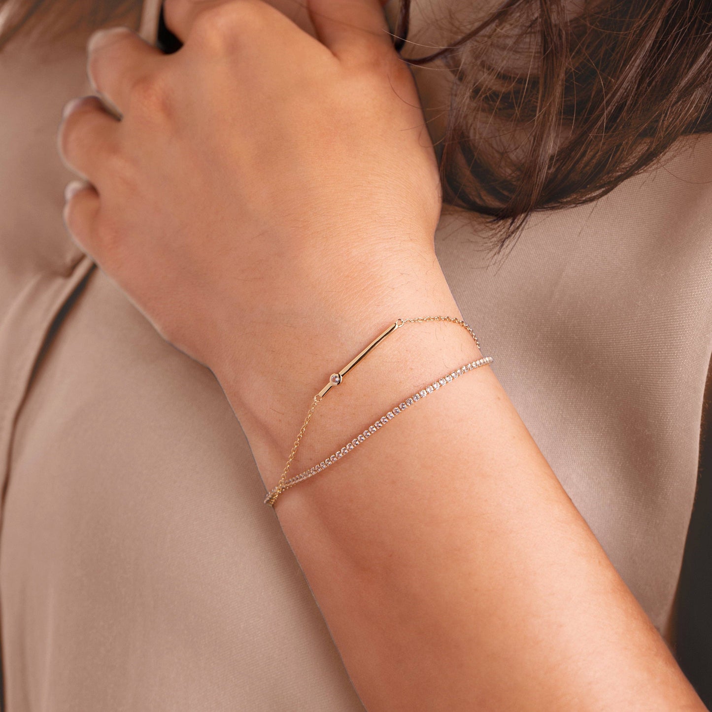 Close-up of a person's wrist wearing multiple gold bracelets on a neutral background