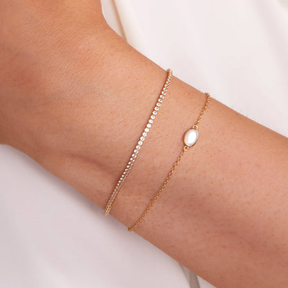 Gold bracelet with a central gemstone on a wrist against a light background