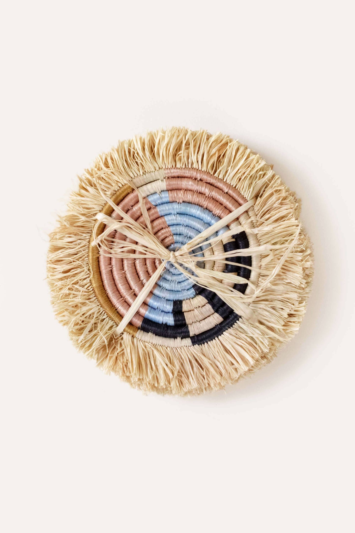 Round woven coaster with colorful concentric circle design on a white background