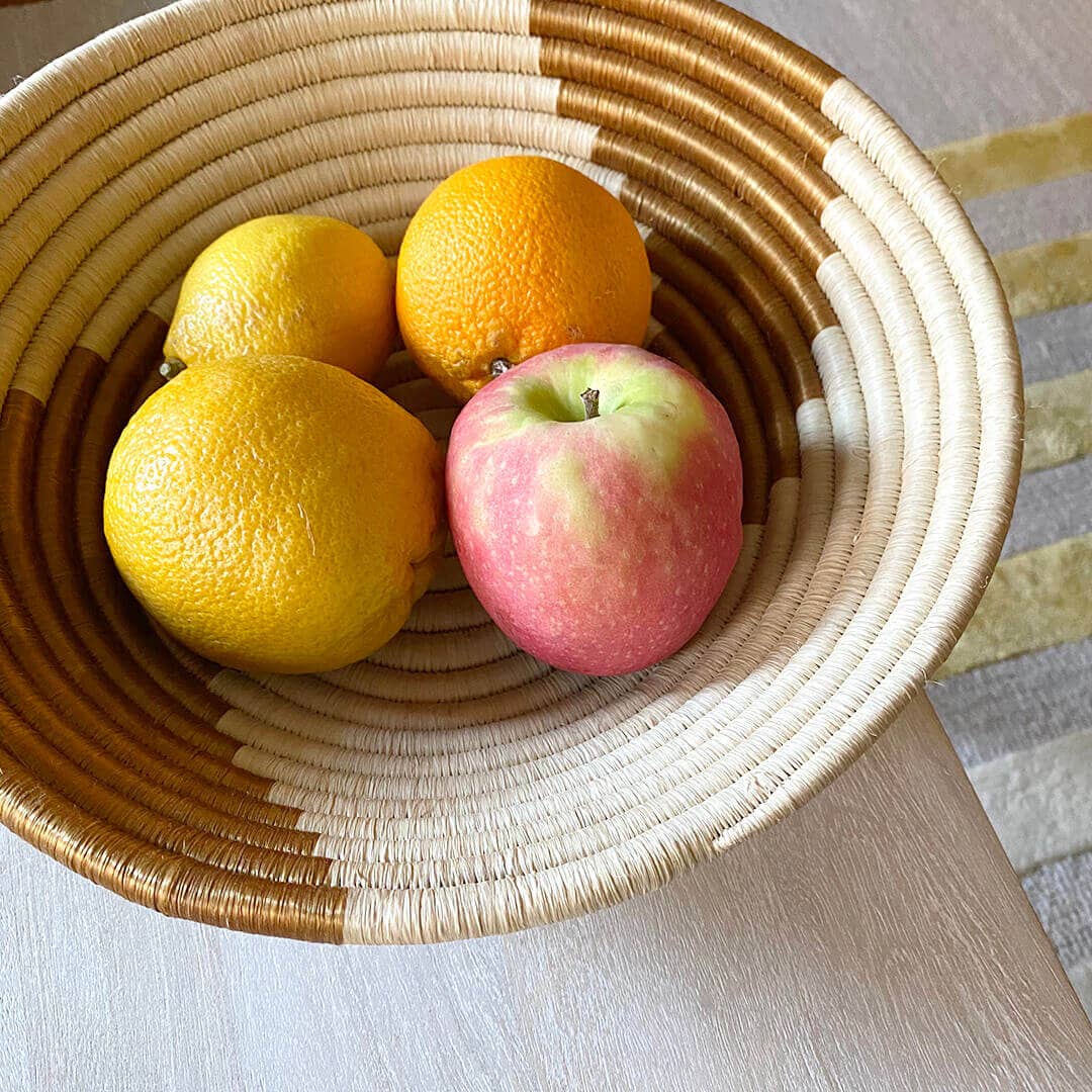 Fruit including lemons and an apple in a woven basket on a light surface.