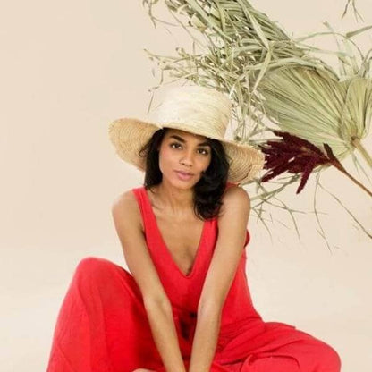 Woman in a red dress and straw hat sitting with dried plants on a beige background