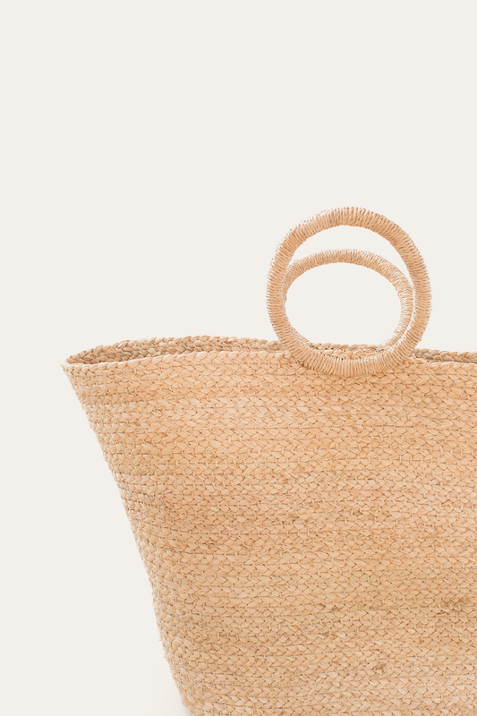 Close-up of a woven straw bag with circular handles on a light beige background