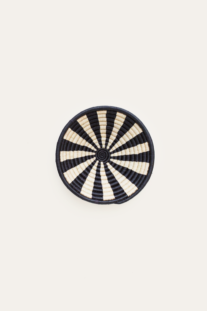 Round woven basket with black and white striped pattern on a beige background