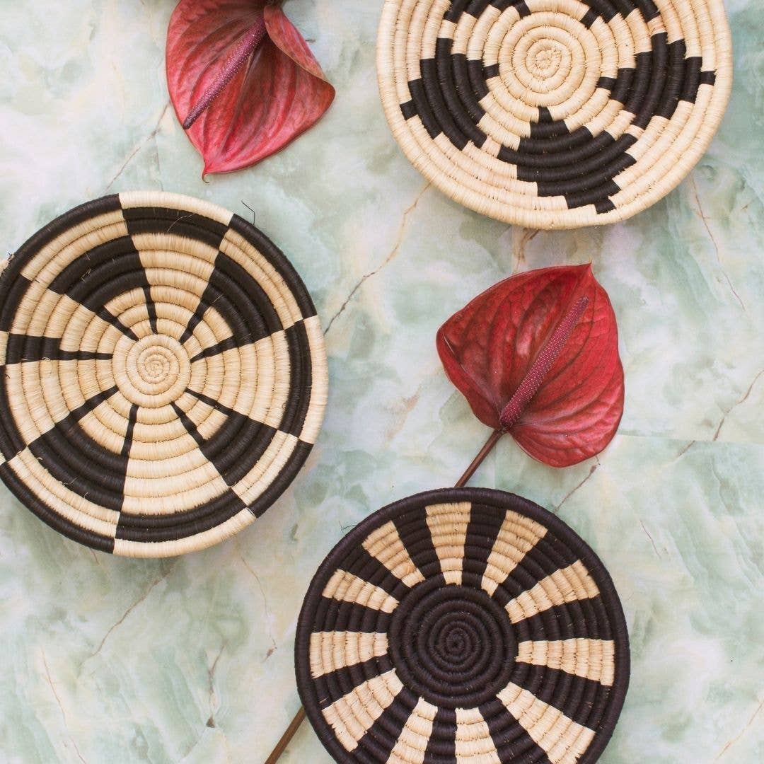 Three woven coasters with black and beige patterns on a textured surface with red leaves.