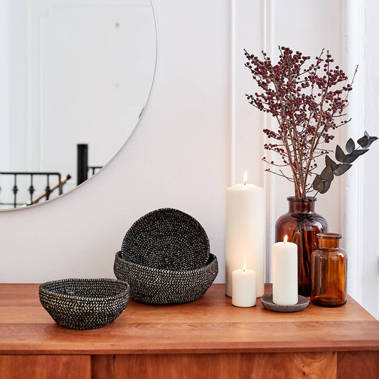Decorative setup with black beaded bowls, candles, and a vase on a wooden surface.