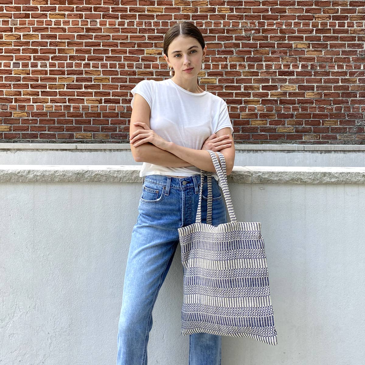 Person holding a striped tote bag against a brick wall.
