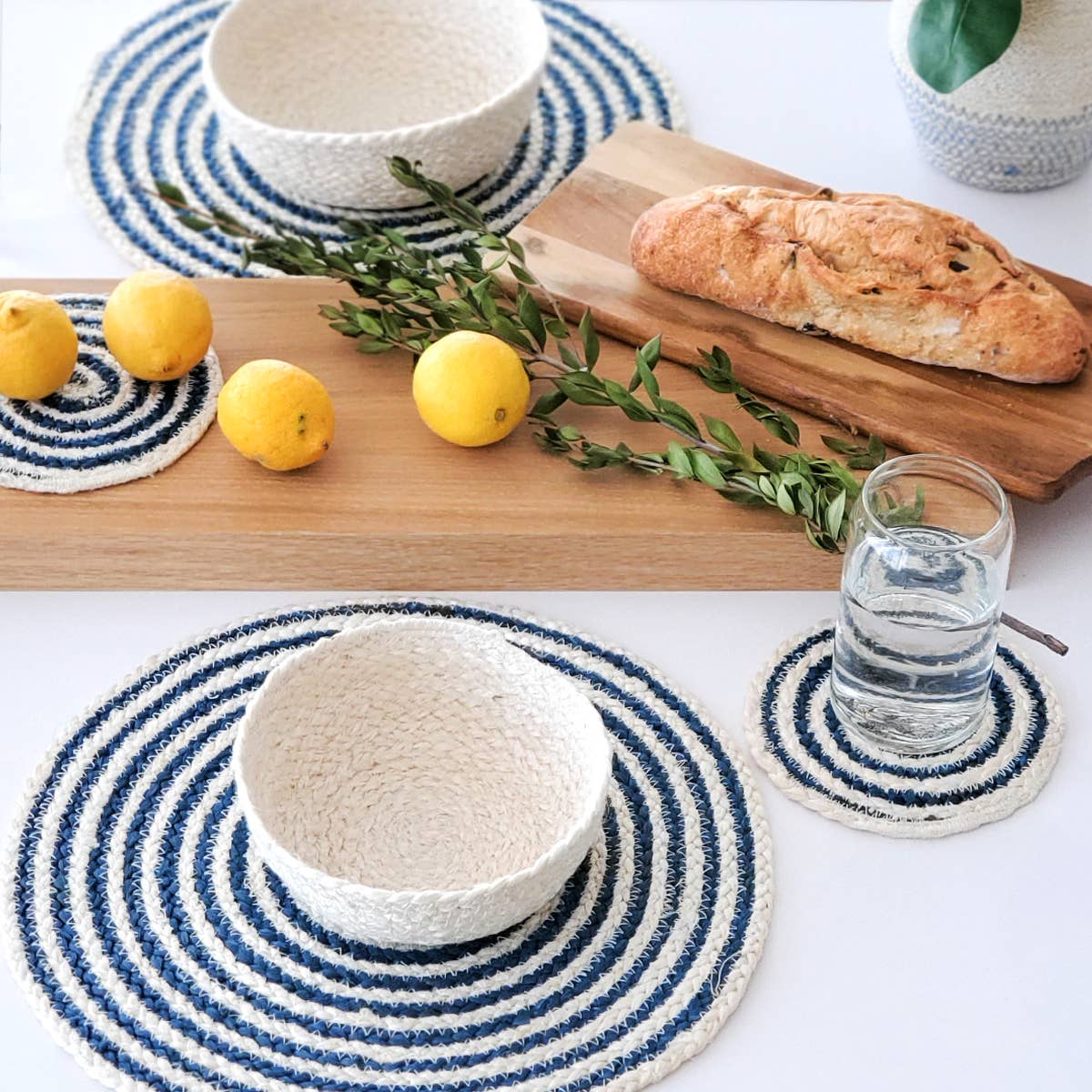 Table setting with blue and white woven coasters, lemons, bread, and a glass of water.